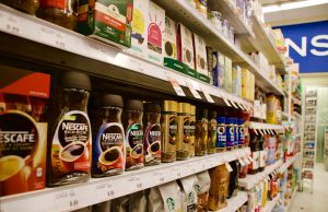 UK E. coli Outbreak Hits 211, Kills 1 Prepackaged sandwiches and salads on a supermarket shelf, with a sign indicating a recall due to E. coli contamination