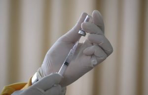 Hamilton Measles Death Sparks Vaccine Gap Warning A nurse holds a measles vaccine vial beside a calendar marked 12-15 months, symbolizing the infant vaccination window.