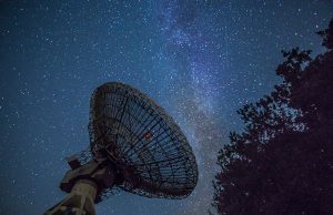 Scientists Explain 1977 Wow! Signal as Stellar Event A radio telescope dish points toward the night sky, capturing a bright burst of light from a distant molecular cloud.
