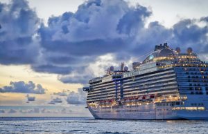 Norovirus Outbreak Hits MS Iona Cruise Ship in Belgium Medical staff in ship infirmary tend seated passengers with IV drips as cleaning crew disinfects railings under bright hallway lights.