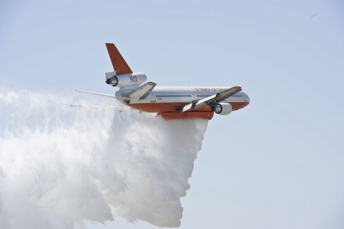 A firefighting plane drops water over a blazing Montana wildfire near a lake