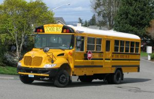 School Bus Crash Kills Two, Injures 17 in England Overturned yellow school bus on a road in The Wirral, England, with emergency responders and debris visible around the crash site.