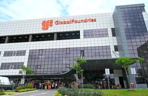 GlobalFoundries Unveils $6B Plan to Expand Chip Production Engineers in cleanroom suits walk past gleaming silicon wafer fabrication equipment at a new GlobalFoundries plant under construction.