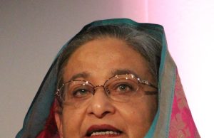 Sheikh Hasina Resigns After July Uprising Sheikh Hasina speaking at a podium with Bangladesh flag in background during a political event.